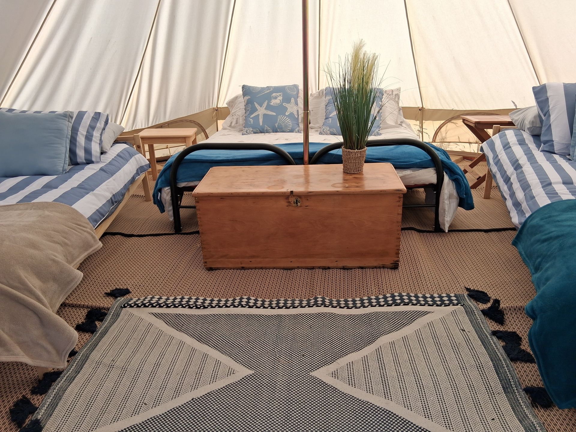 Cozy tent interior with blue-striped lounge cushions, wooden chest table, woven rugs, and pillows