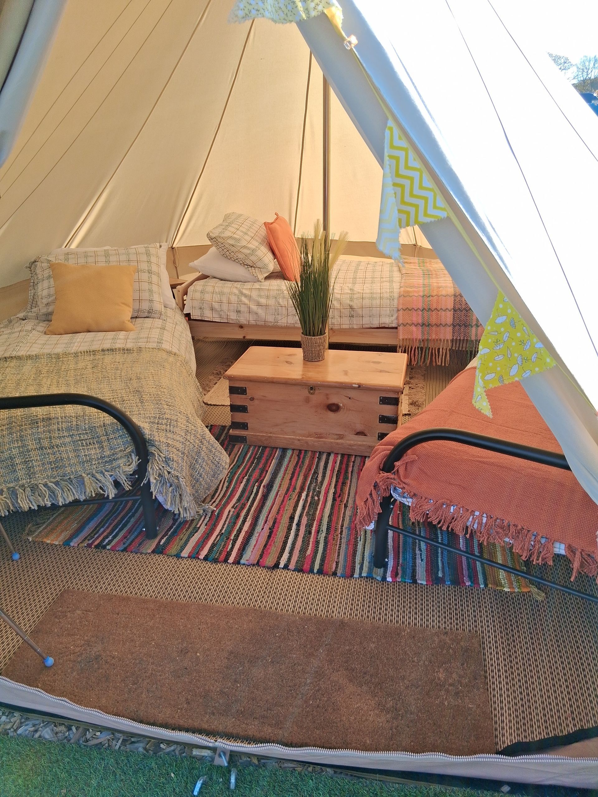 Cozy tent interior with patterned rugs, cushions, wooden crates, and a small plant on the floor