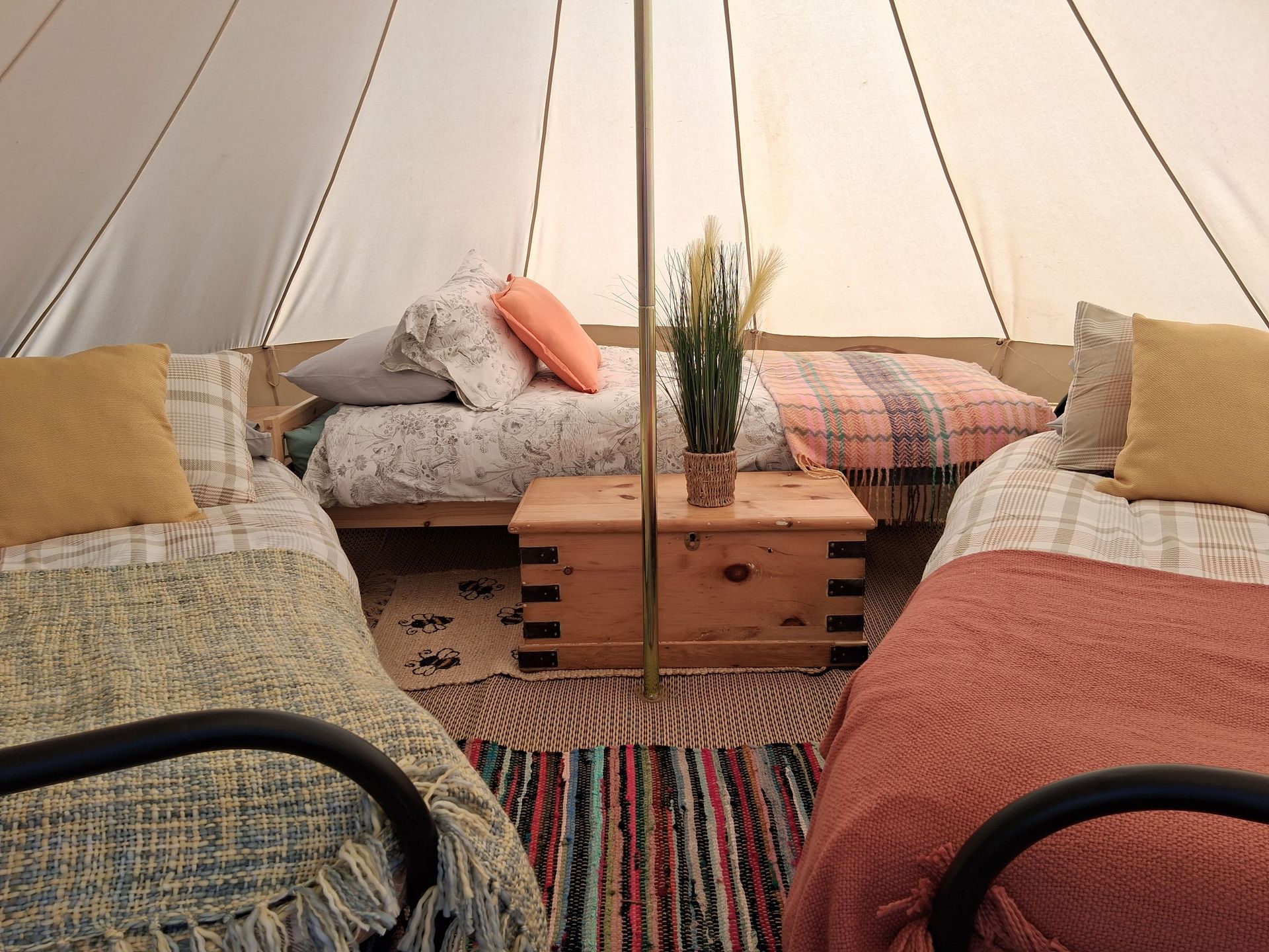 Cozy tent interior with two beds, colorful rugs, a wooden table, and soft cushions.