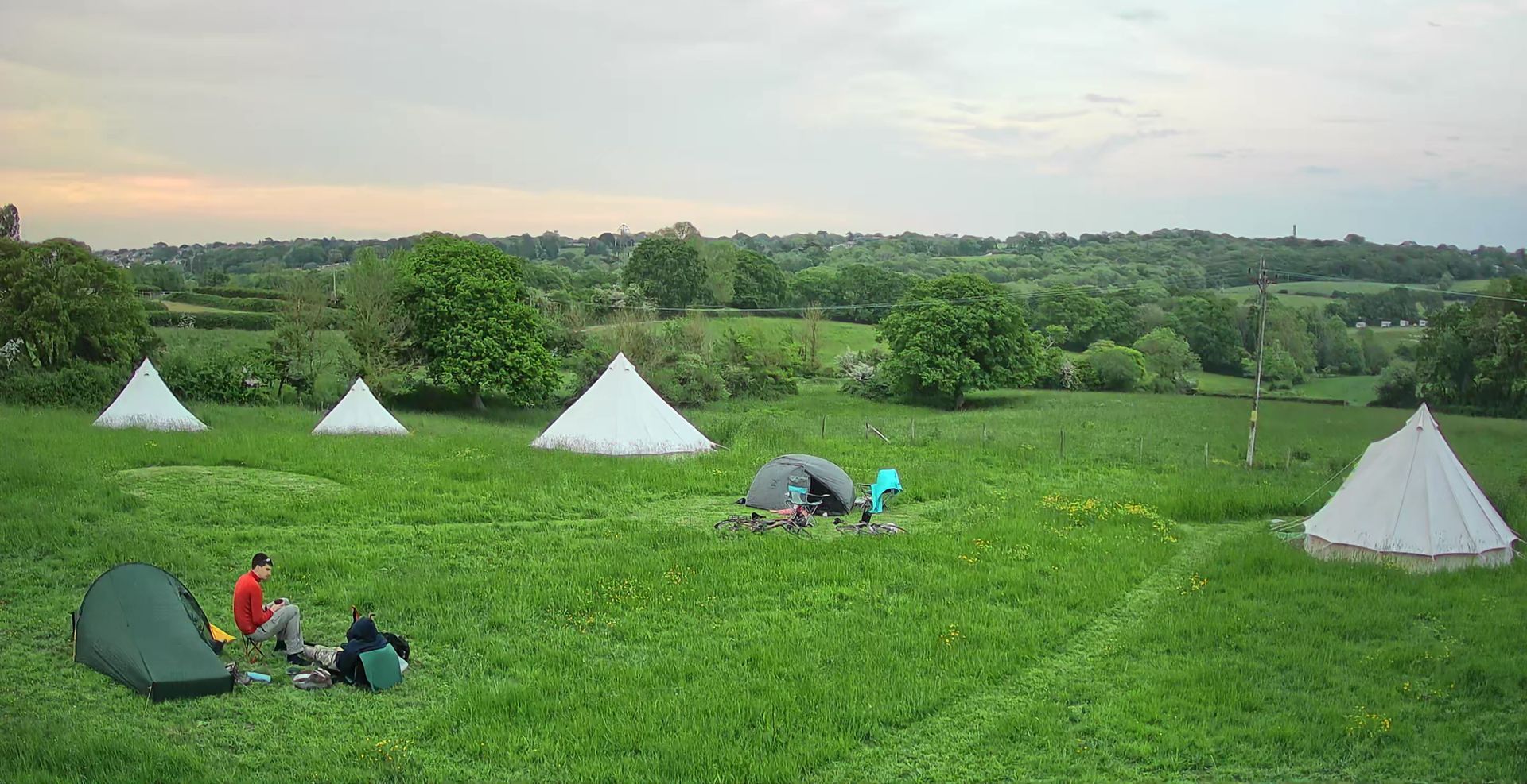People camping in a green field with white tents under a cloudy sky