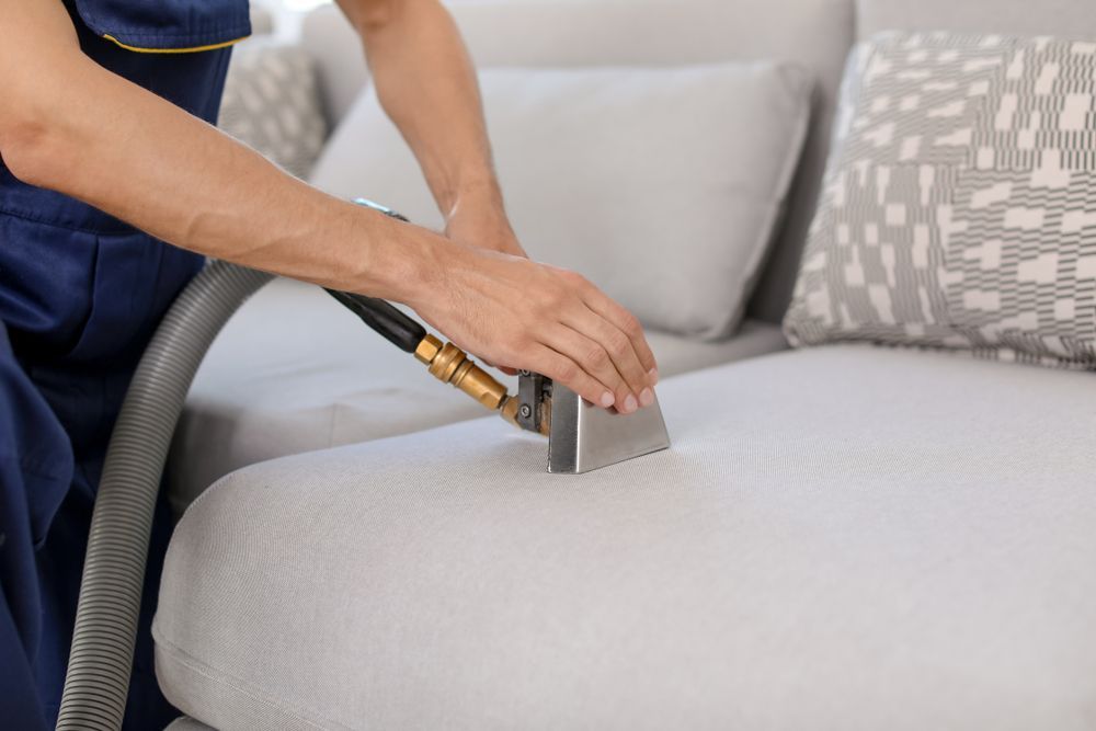 A Person is Cleaning a Couch With a Vacuum Cleaner — We Clean Lounges In Bli Bli, QLD