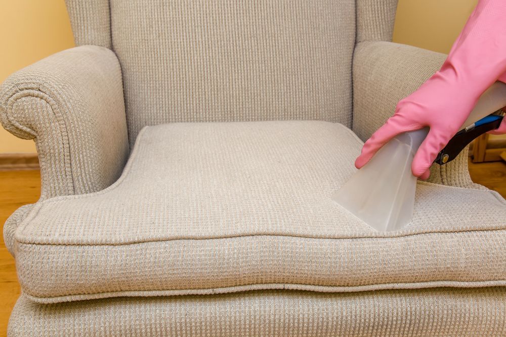A Person Wearing Pink Gloves is Cleaning a Chair With a Vacuum Cleaner — We Clean Lounges In Kawana Waters, QLD