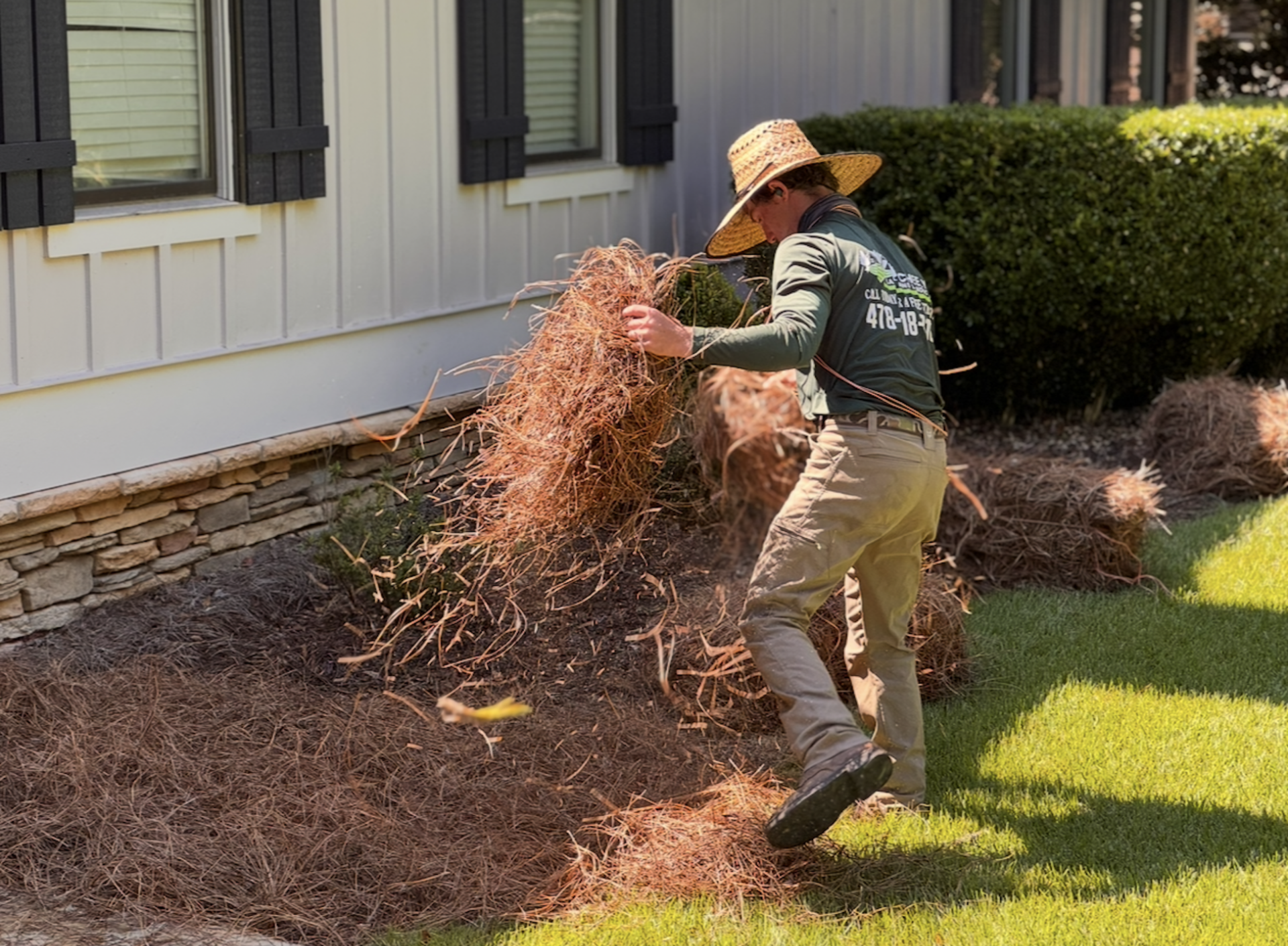 Gardener piling dried leaves near a house beside a hedge and lawn