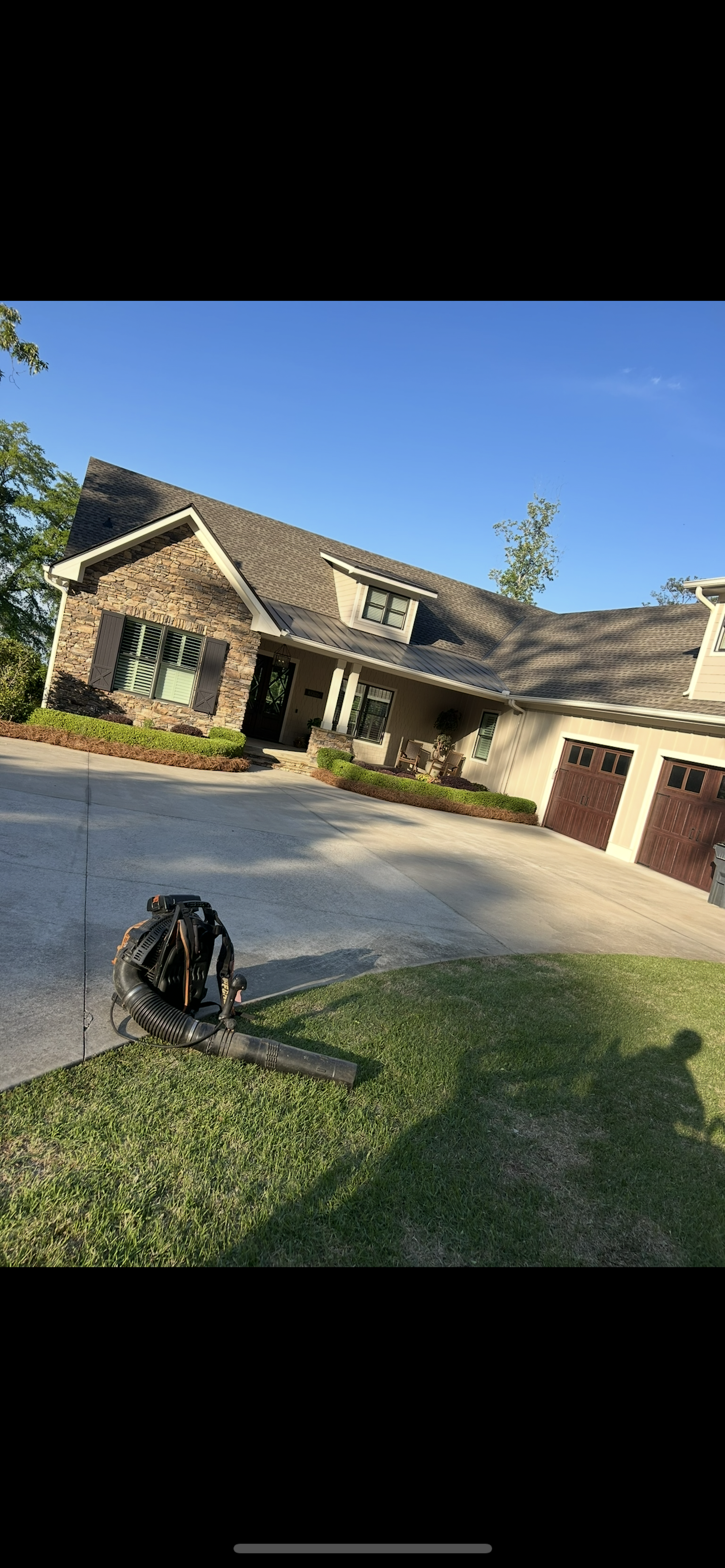 Suburban house with stone facade, driveway, and front lawn under a clear blue sky