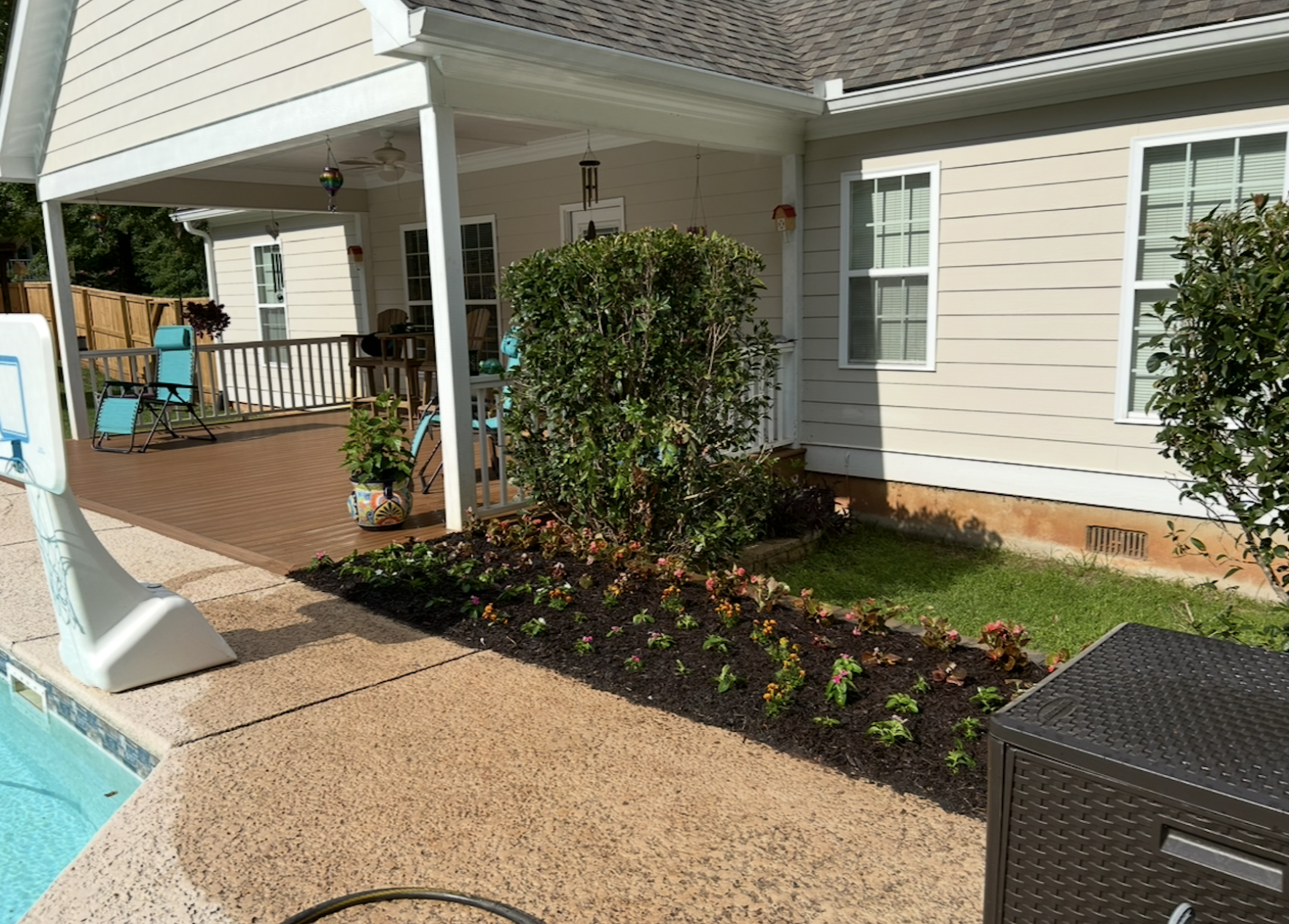 Apartment patio with covered walkway, pool edge, and landscaped flower bed beside beige siding