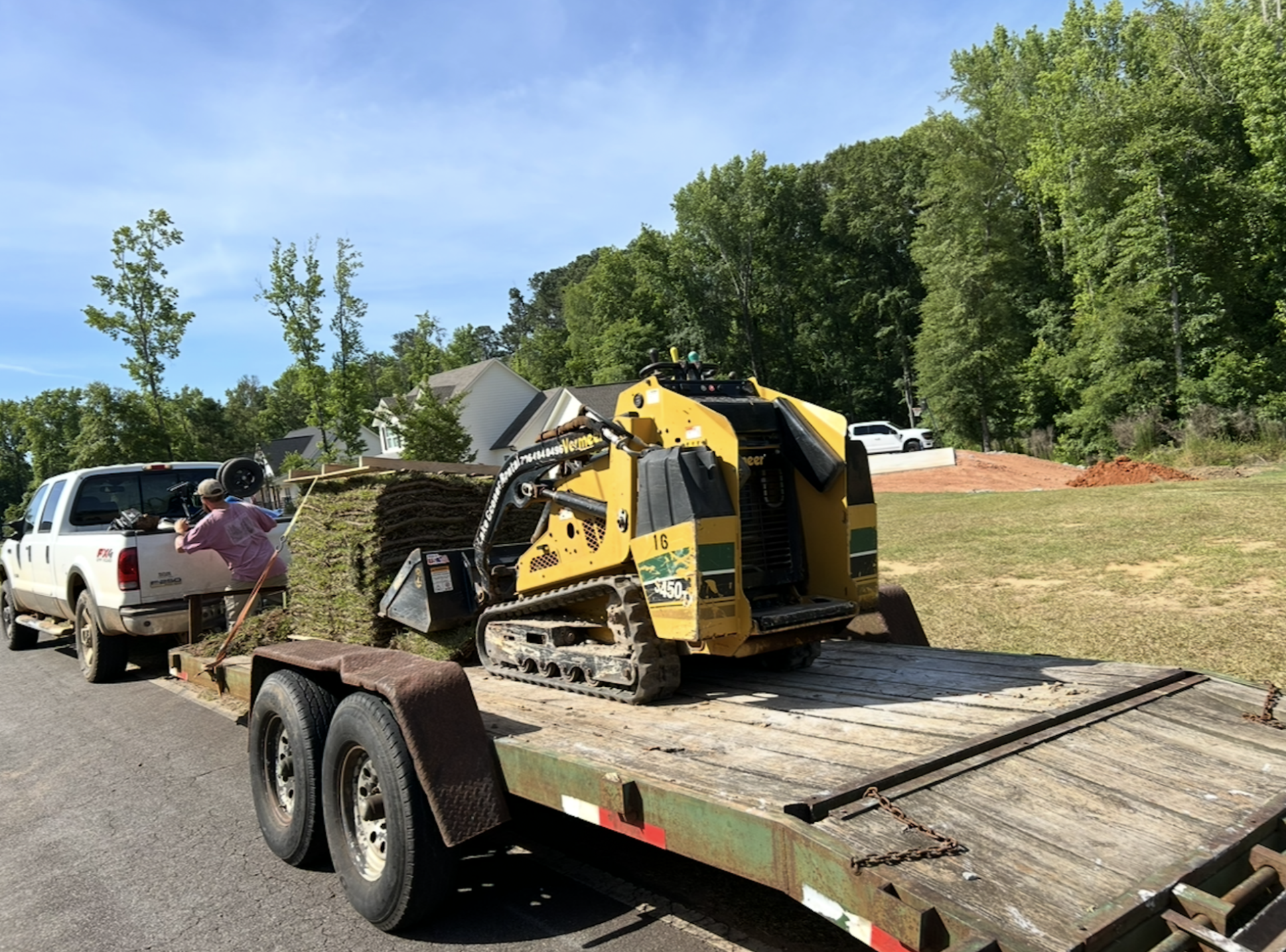 Yellow tractor with a front loader pulling a trailer on a dirt road in a rural field