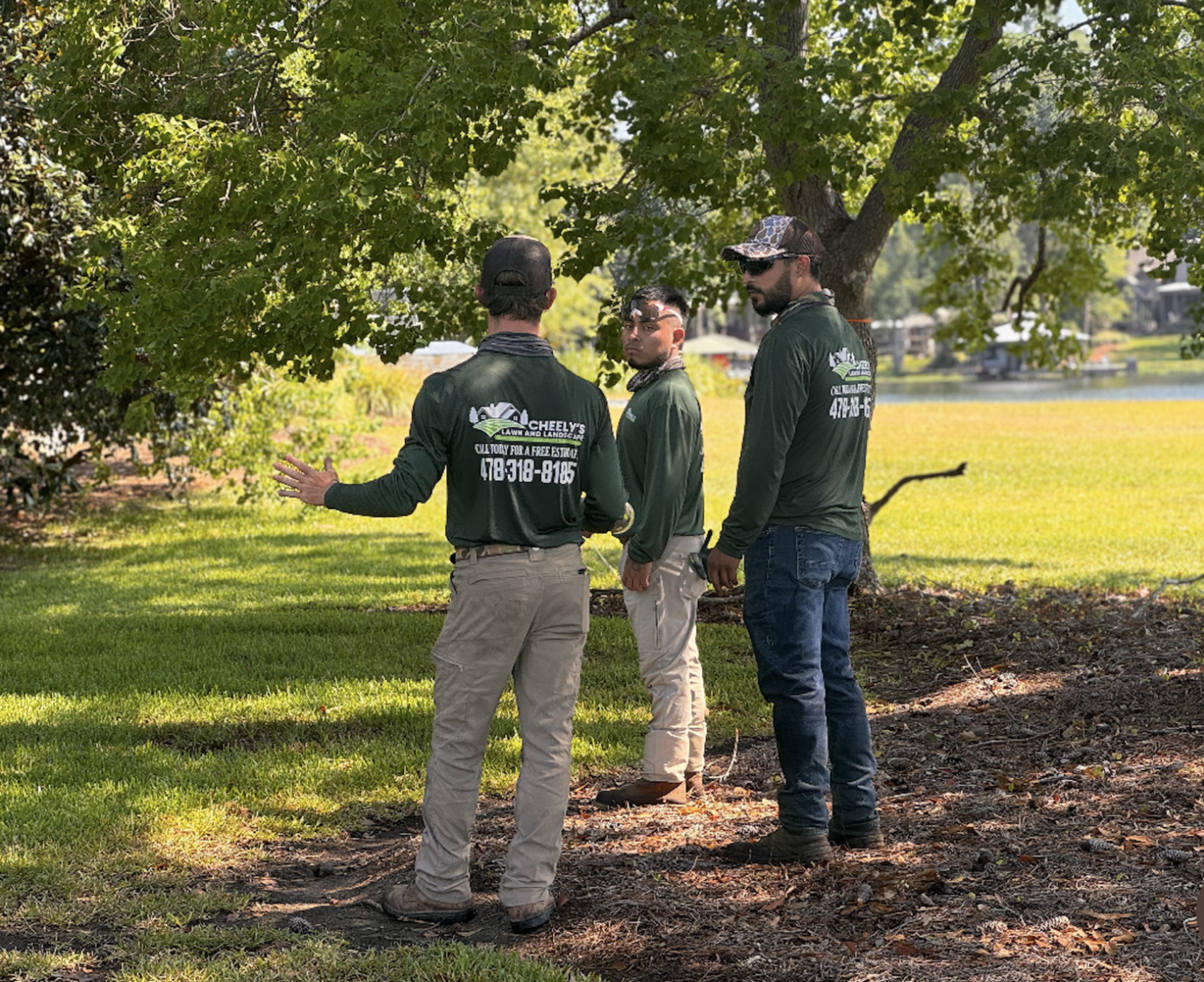Three people standing outdoors on fallen leaves in a sunlit park, talking near trees.