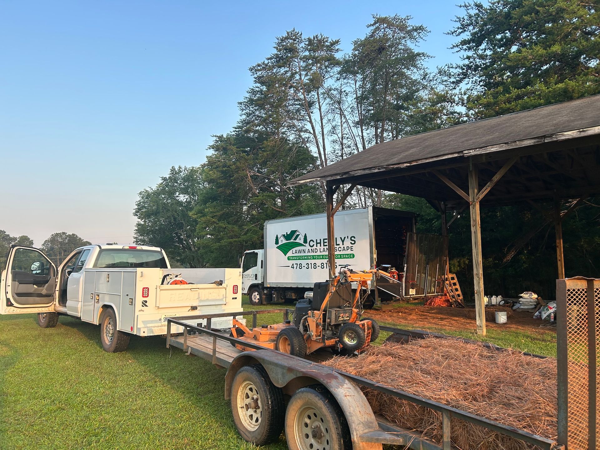 White pickup towing trailer with equipment beside a shed on a rural property