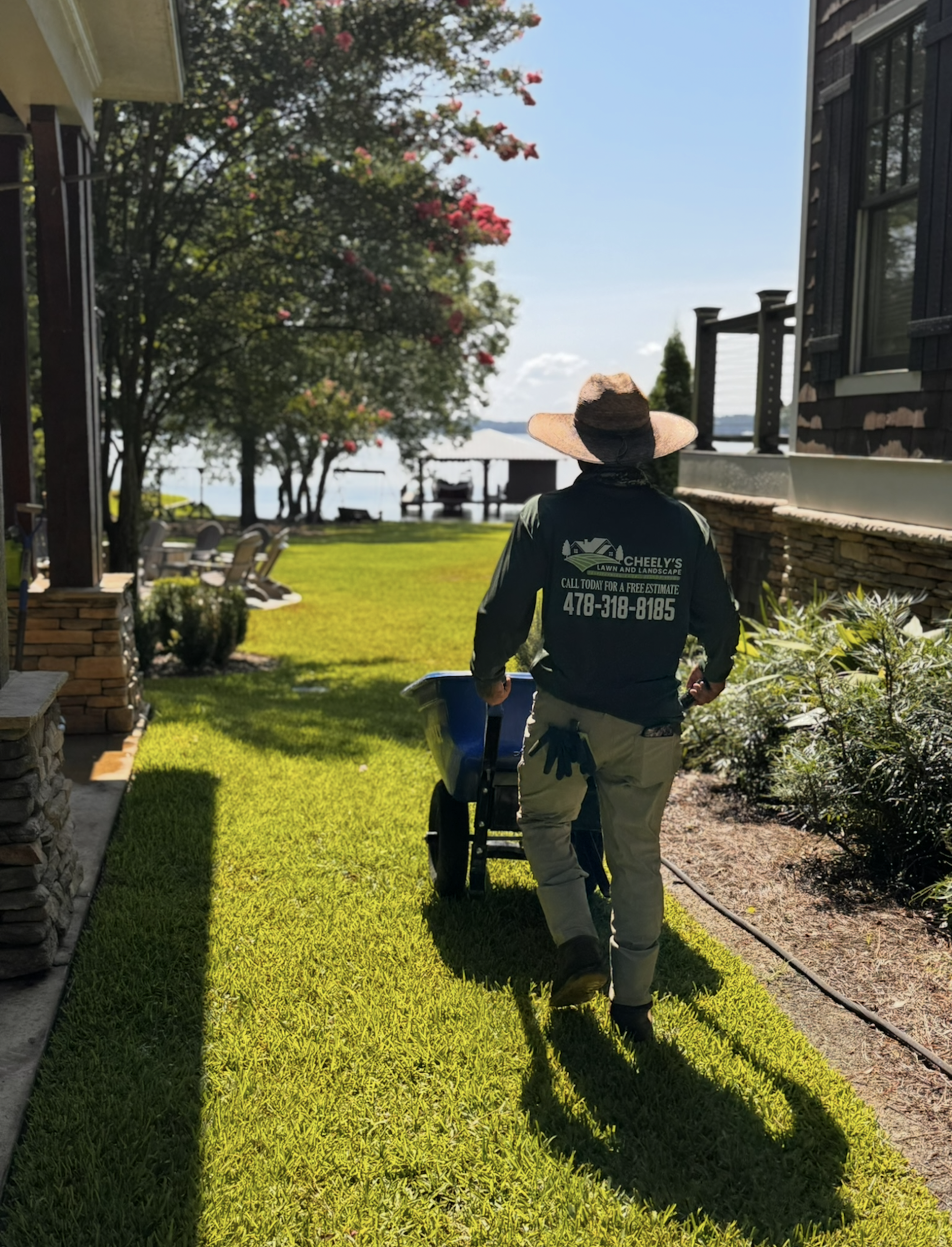 Person pushing a stroller on a sunny lawn beside a waterfront building