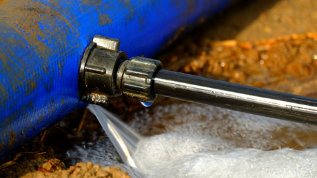 Leaking pipe with a blue end and metal pipe connected, water spraying out.
