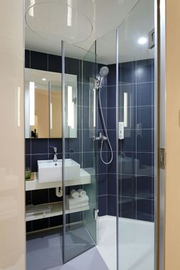 Small modern hotel bathroom with shower, sink, mirror, and towels.