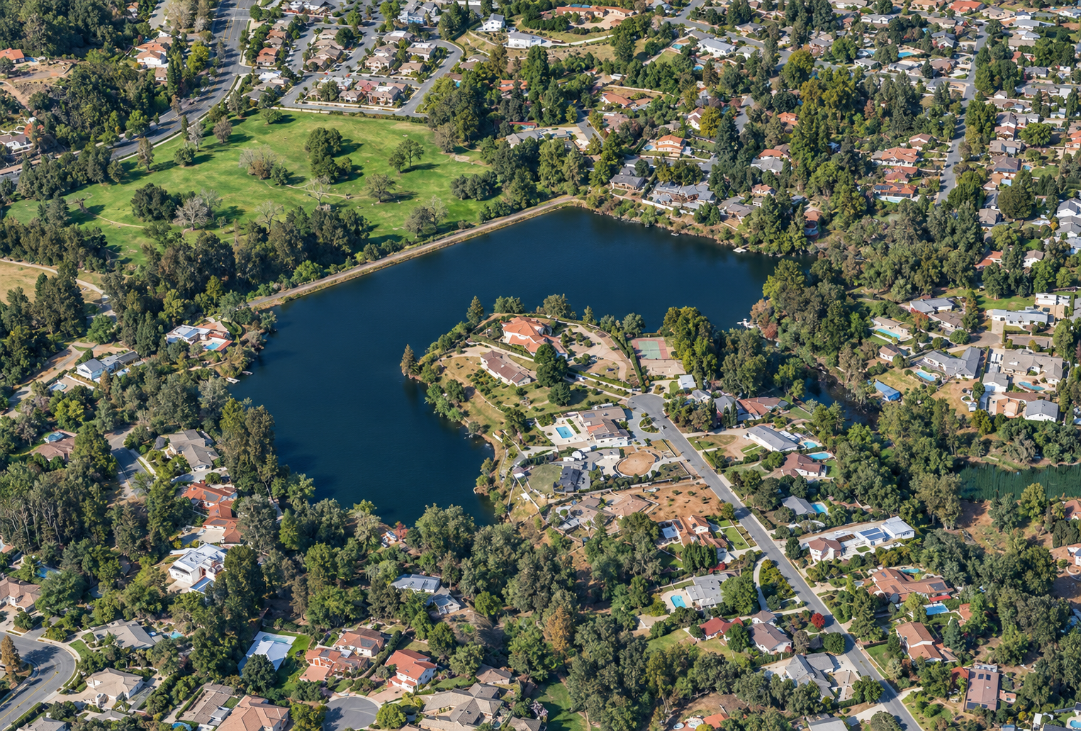 Aerial view of a dark-blue lake surrounded by trees and suburban houses.