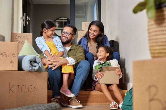 A family is sitting on the steps of their new home holding moving boxes.