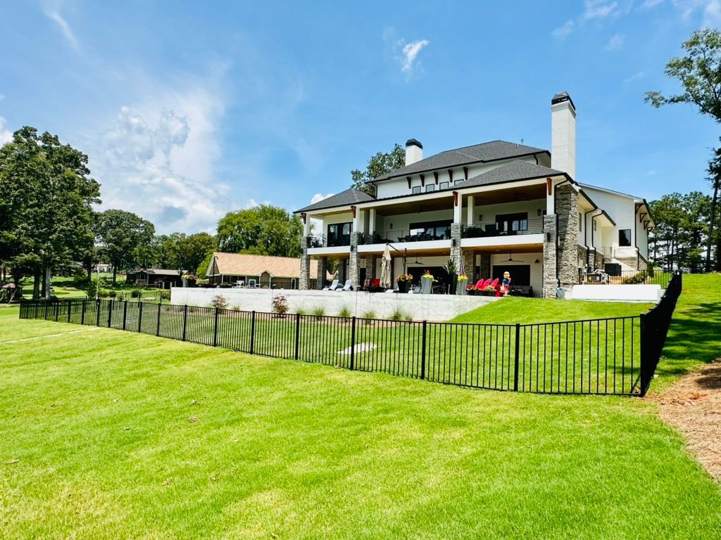 Large white house with black fence, overlooking a green lawn under a blue sky.