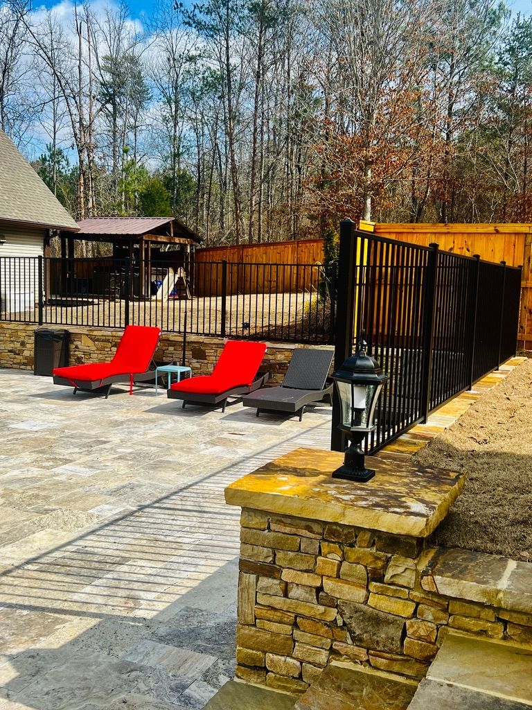 Stone patio with lounge chairs; black fence and forested backdrop.