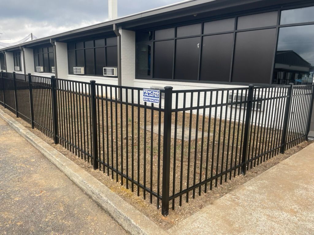 Black metal fence in front of a modern building with dark windows and a paved area.