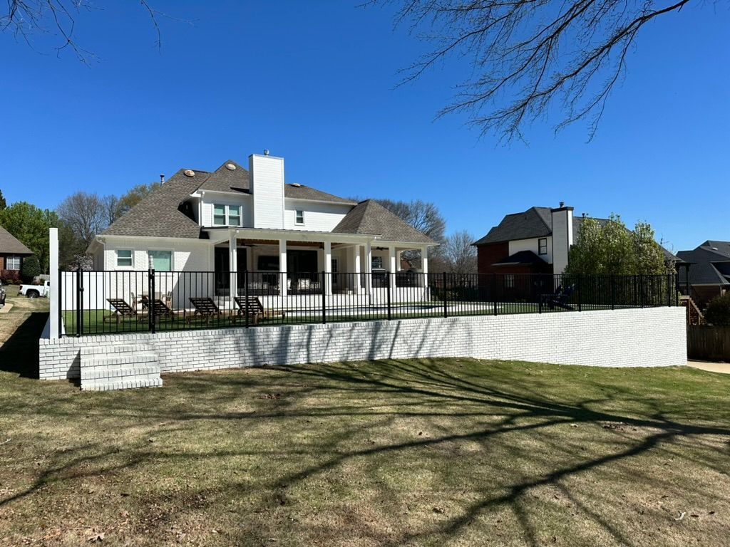 A large white house with a pool and a black fence on a sunny day.
