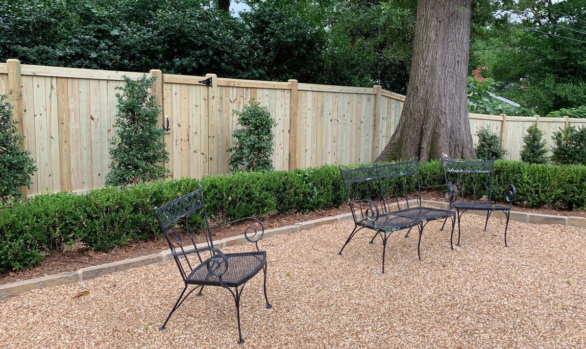 Patio with black metal chairs, gravel ground, and wooden fence.