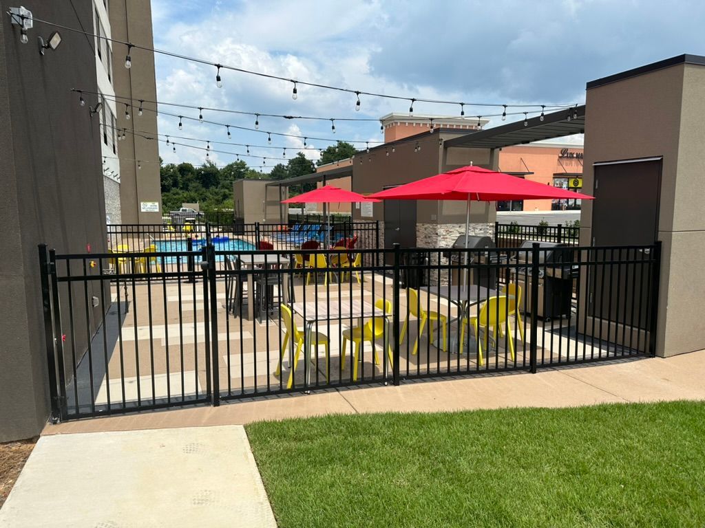 Fenced outdoor patio area with yellow chairs, red umbrellas, and string lights.