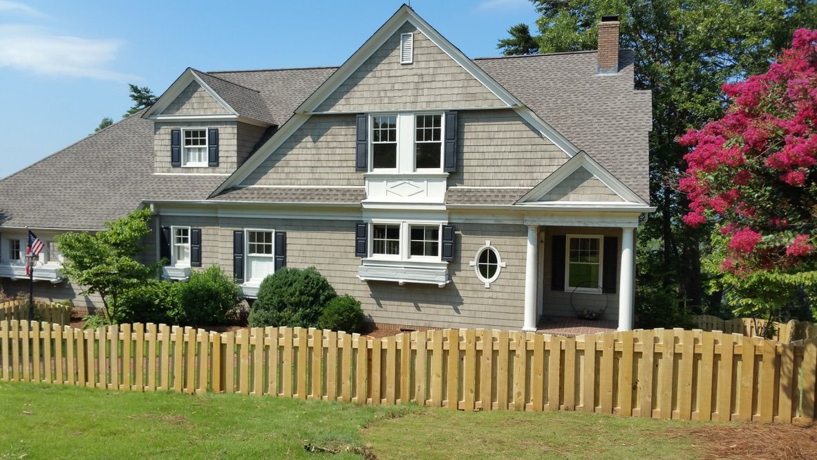 Stone house with wooden picket fence, shrubs, and pink flowering tree.
