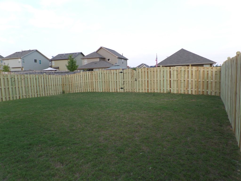 A fenced backyard with green grass and several houses in the background.