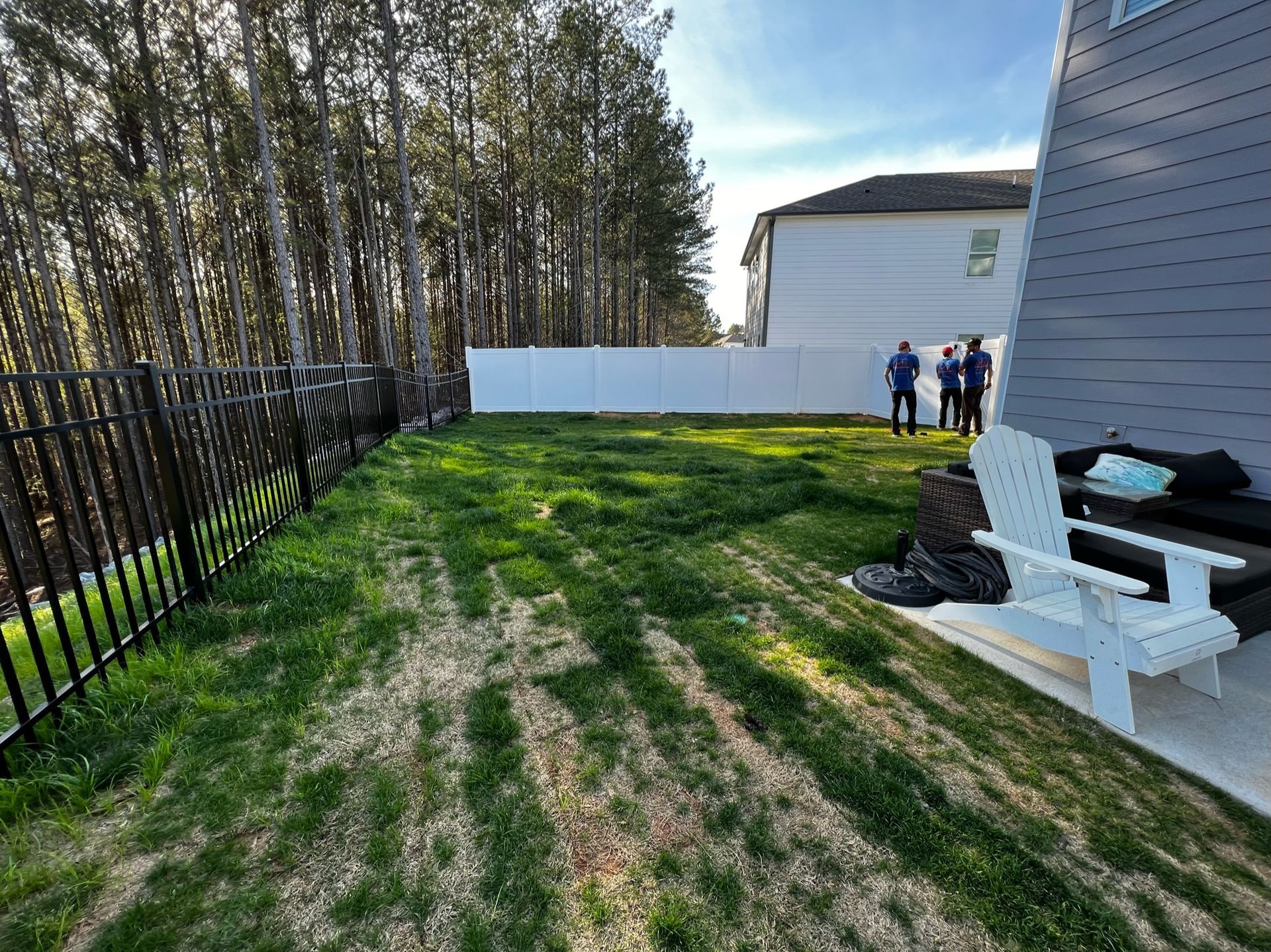 Backyard with lawn, fences, trees, and people standing near a house.