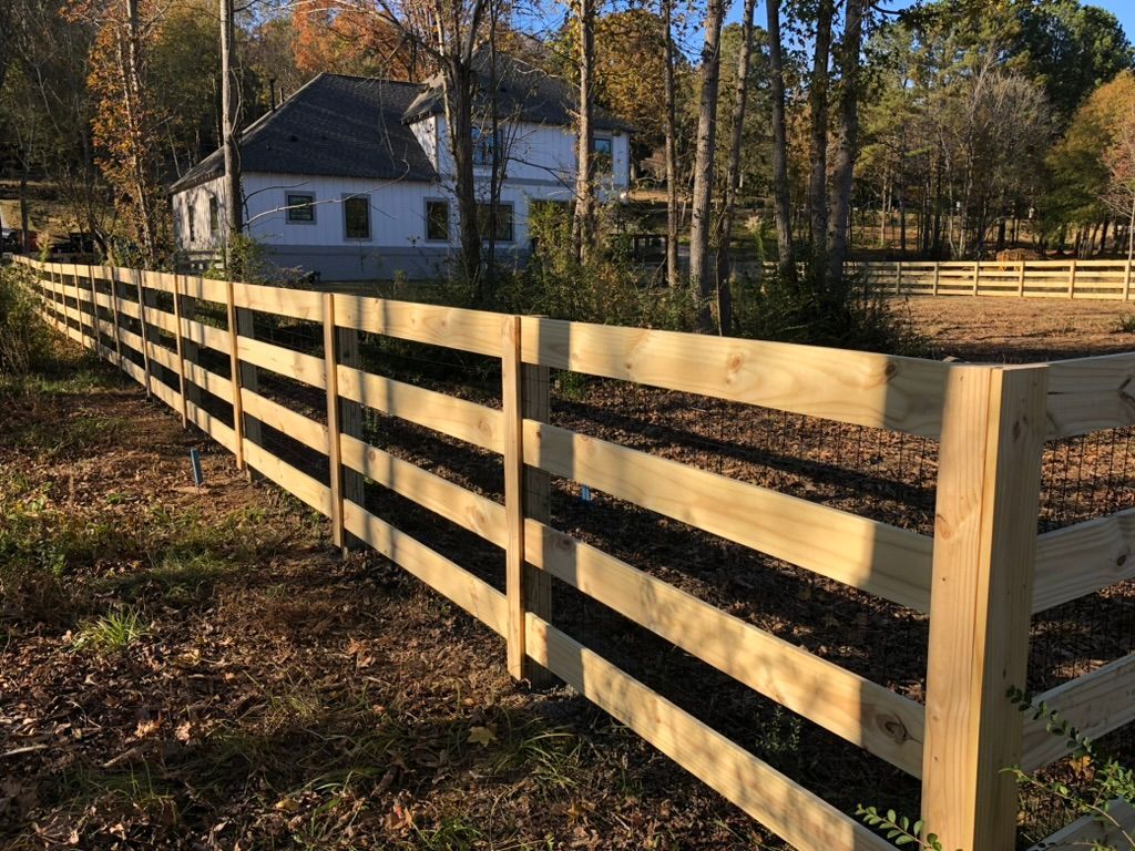 Wooden fence surrounding a yard, with a house visible in the background. Autumn trees are nearby.