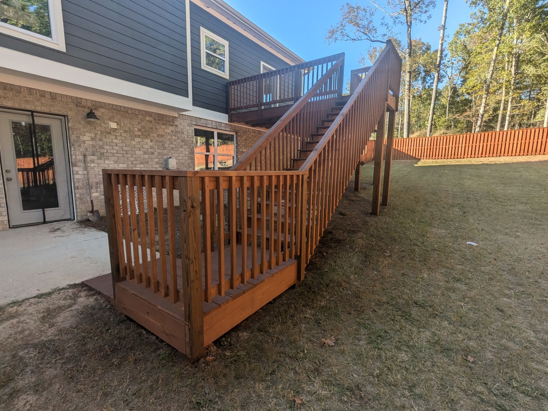 Wooden staircase leading up to a deck of a two-story house, set in a grassy backyard.