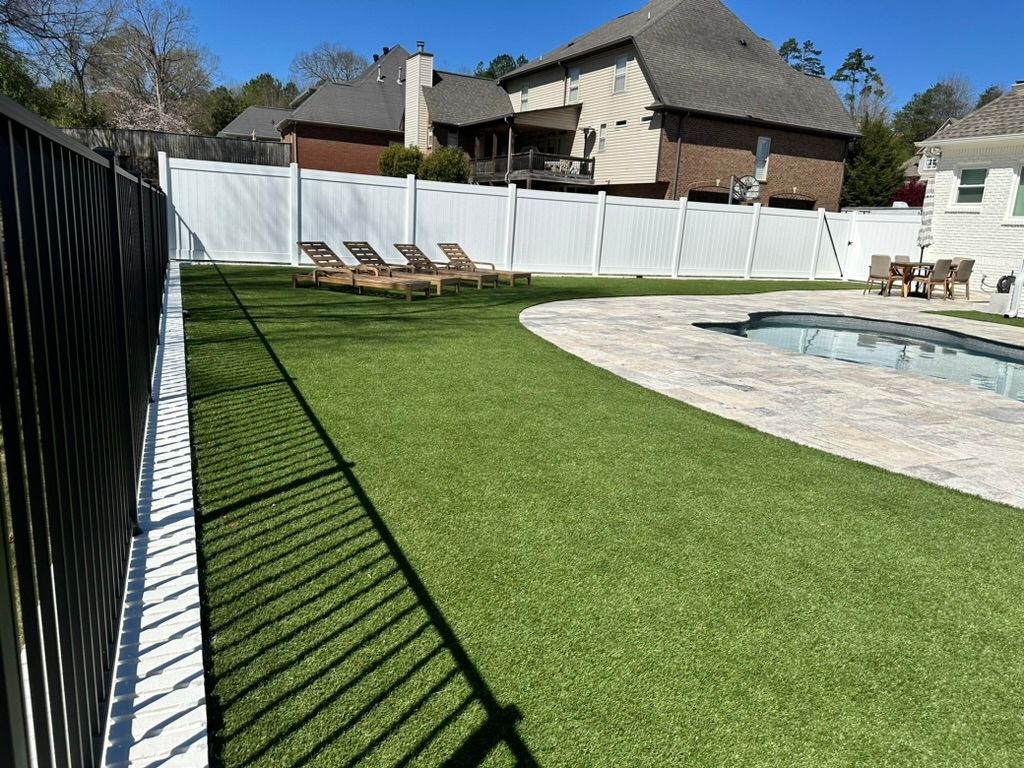 Backyard with green turf, white fence, pool, and lounge chairs.