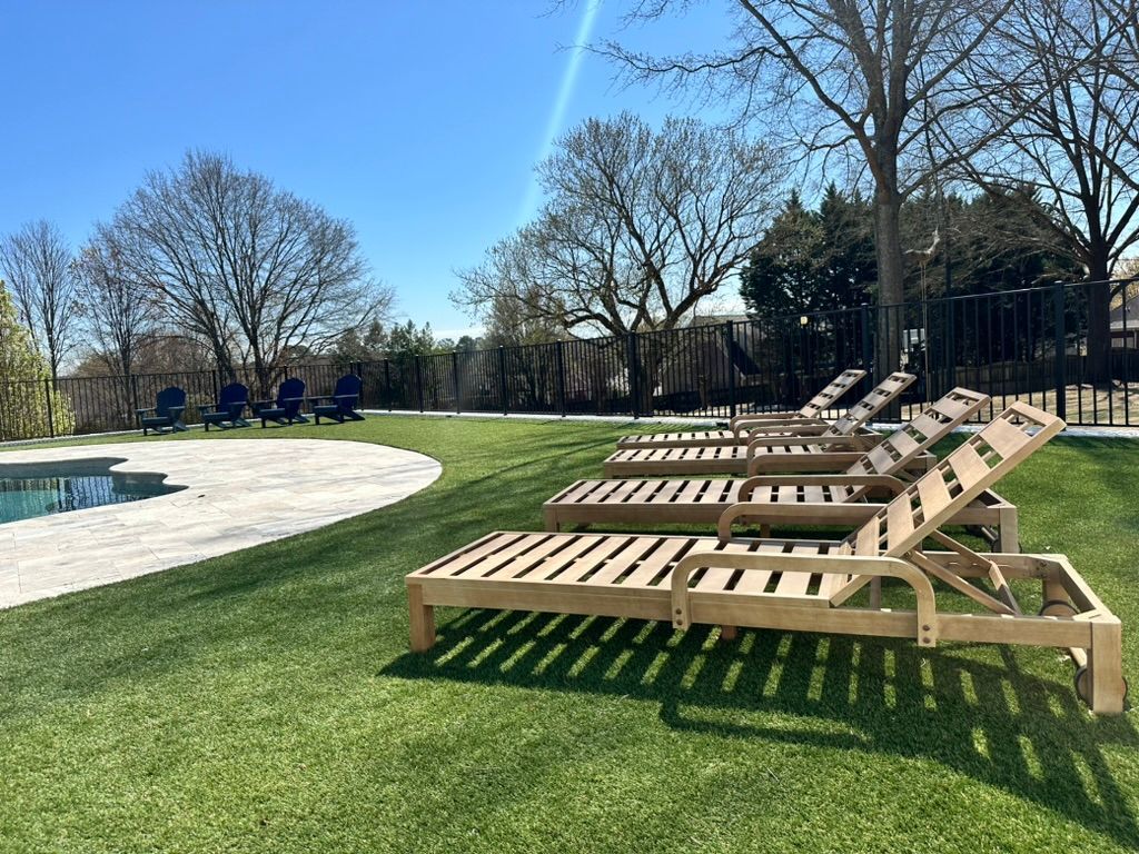 Wooden lounge chairs on a grassy lawn beside a pool on a sunny day.