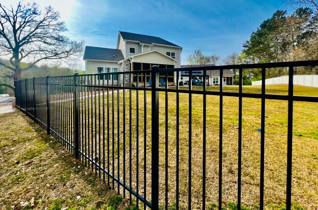 Black metal fence in front of a two-story house with a backyard. Blue sky and sunny day.
