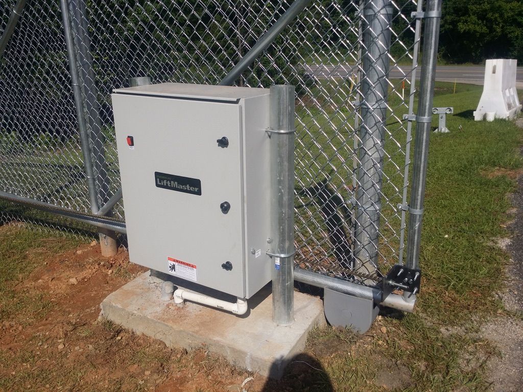 Gray control box on a concrete pad next to a chain link fence.