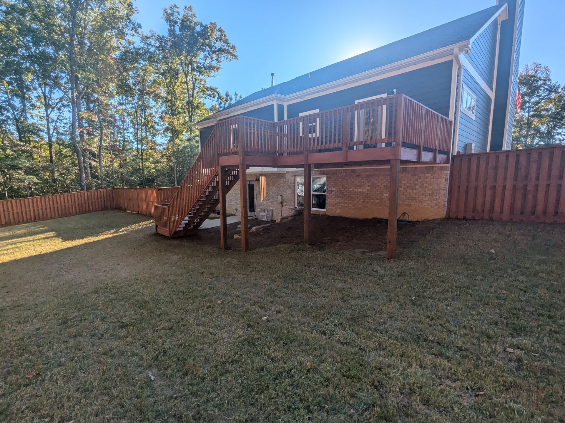 Backyard with a raised wooden deck, stairs, and a brown fence surrounding a grassy area.