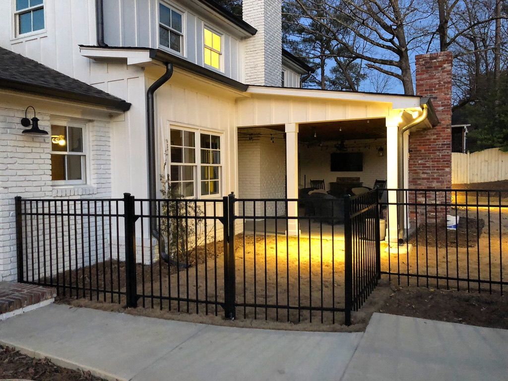 Black fence encloses a backyard patio with white house and red brick chimney.