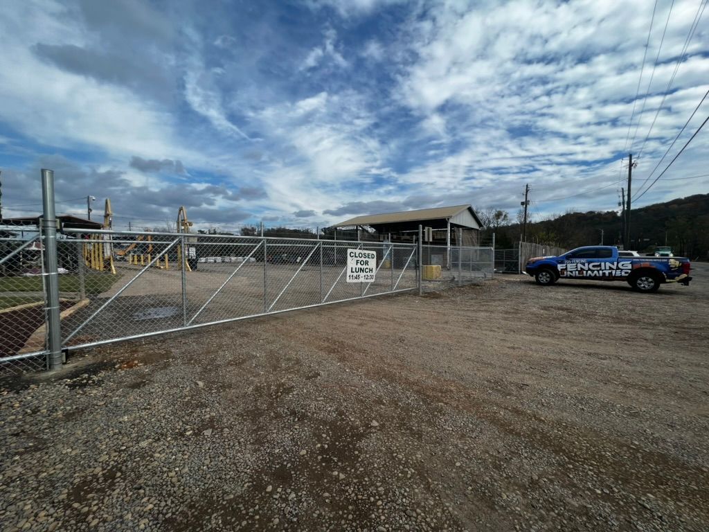 Chain-link fence gate with a police vehicle parked outside, cloudy sky overhead.
