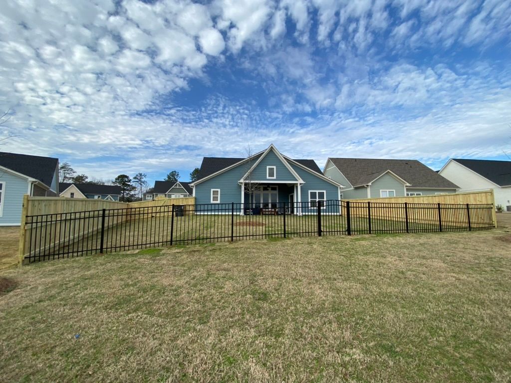 Backyard view of blue house with black metal fence and wooden fence, blue sky.