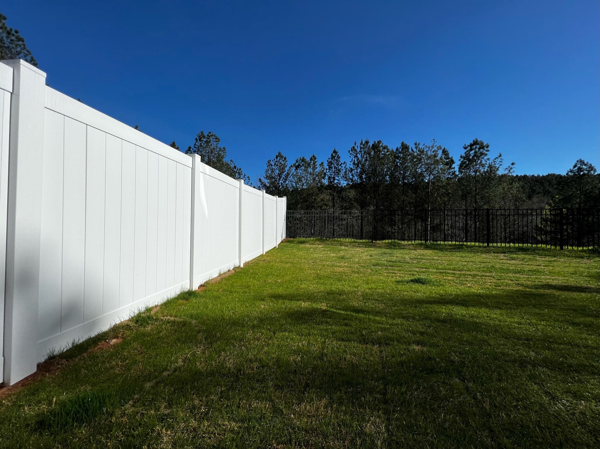 White vinyl fence bordering a green grassy lawn under a clear blue sky.