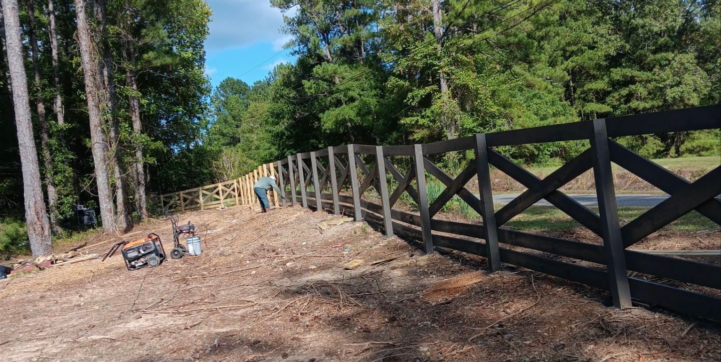 A dark wooden fence under construction with a person working on the dirt embankment.