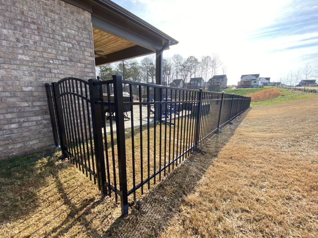 Black metal fence bordering a yard next to a brick building.