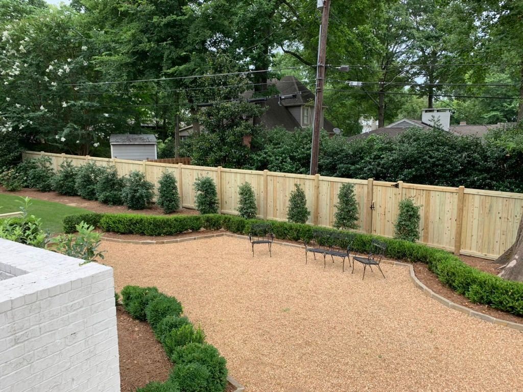 Wooden fence with landscaped shrubs, gravel path, and small trees in a backyard setting.
