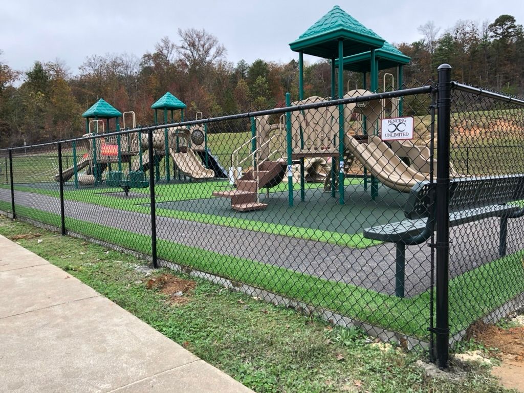 Playground with green structures, brown slides, and black fence on green play surface.