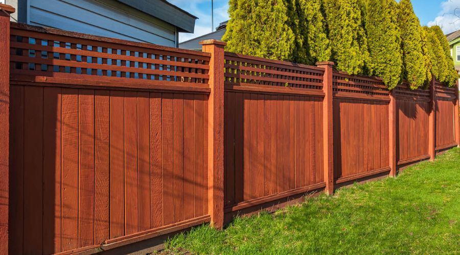 Red wooden privacy fence with decorative lattice in a backyard
