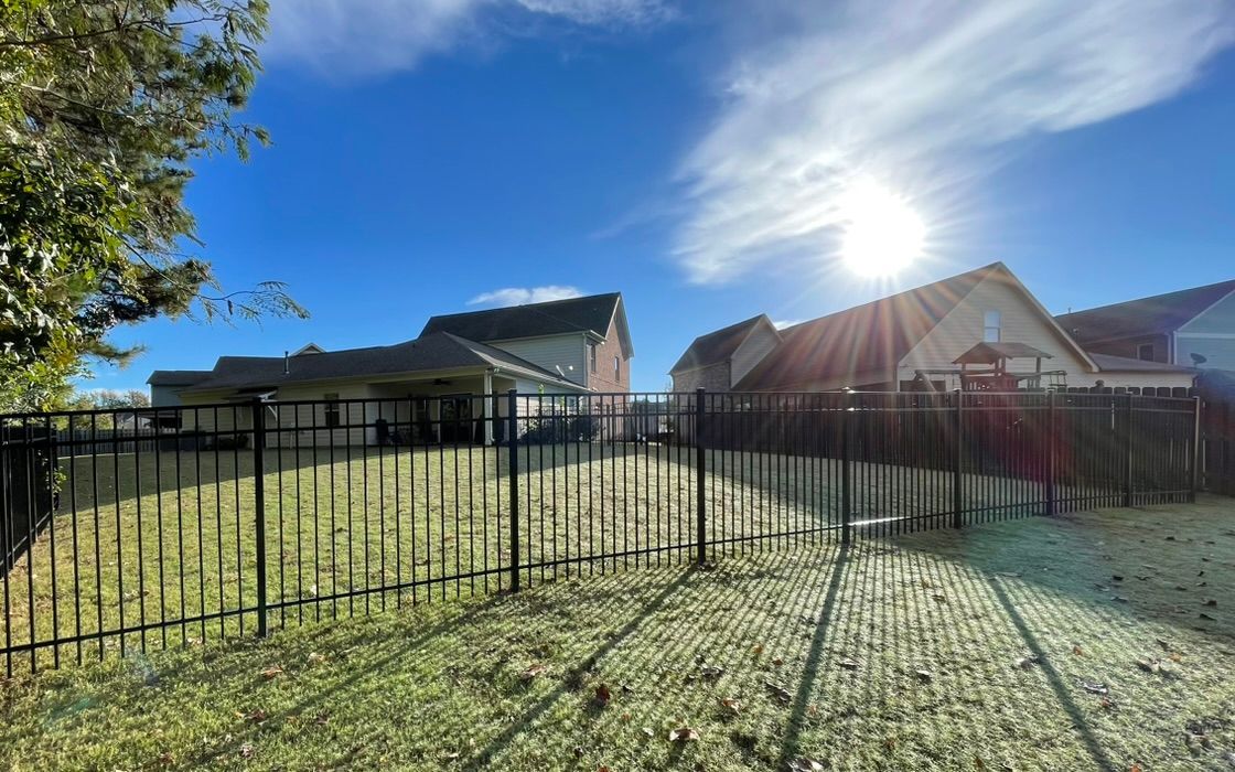 Black fenced backyard with houses under a bright sun and blue sky.