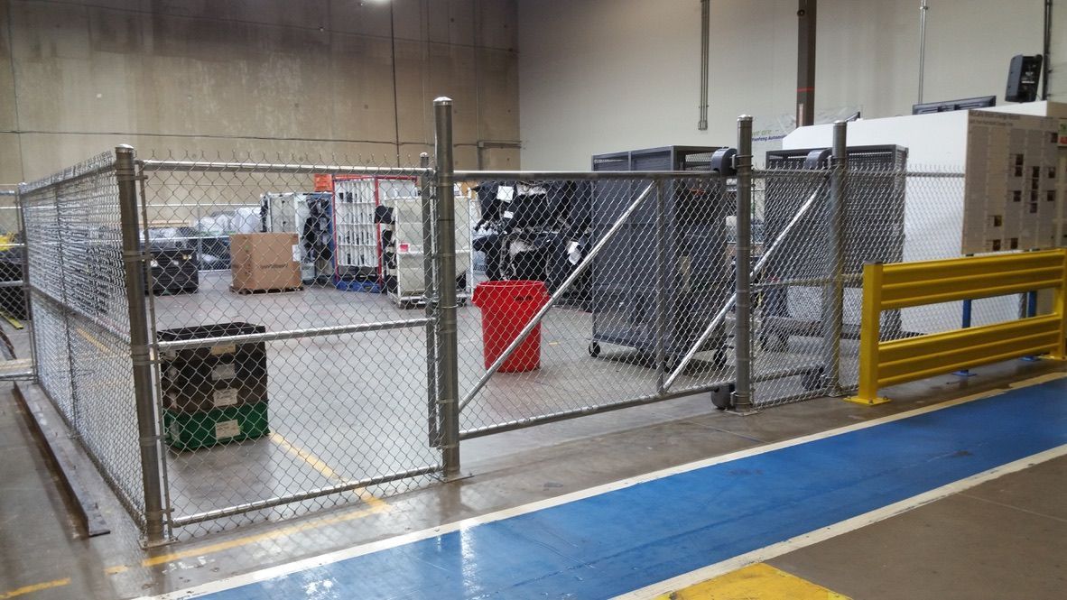 A fenced area in an industrial setting, with storage bins, a red bin, and a yellow safety barrier.
