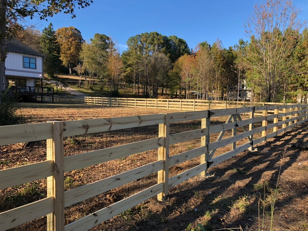 Wooden fence in a field, with trees and a house in the background on a sunny day.