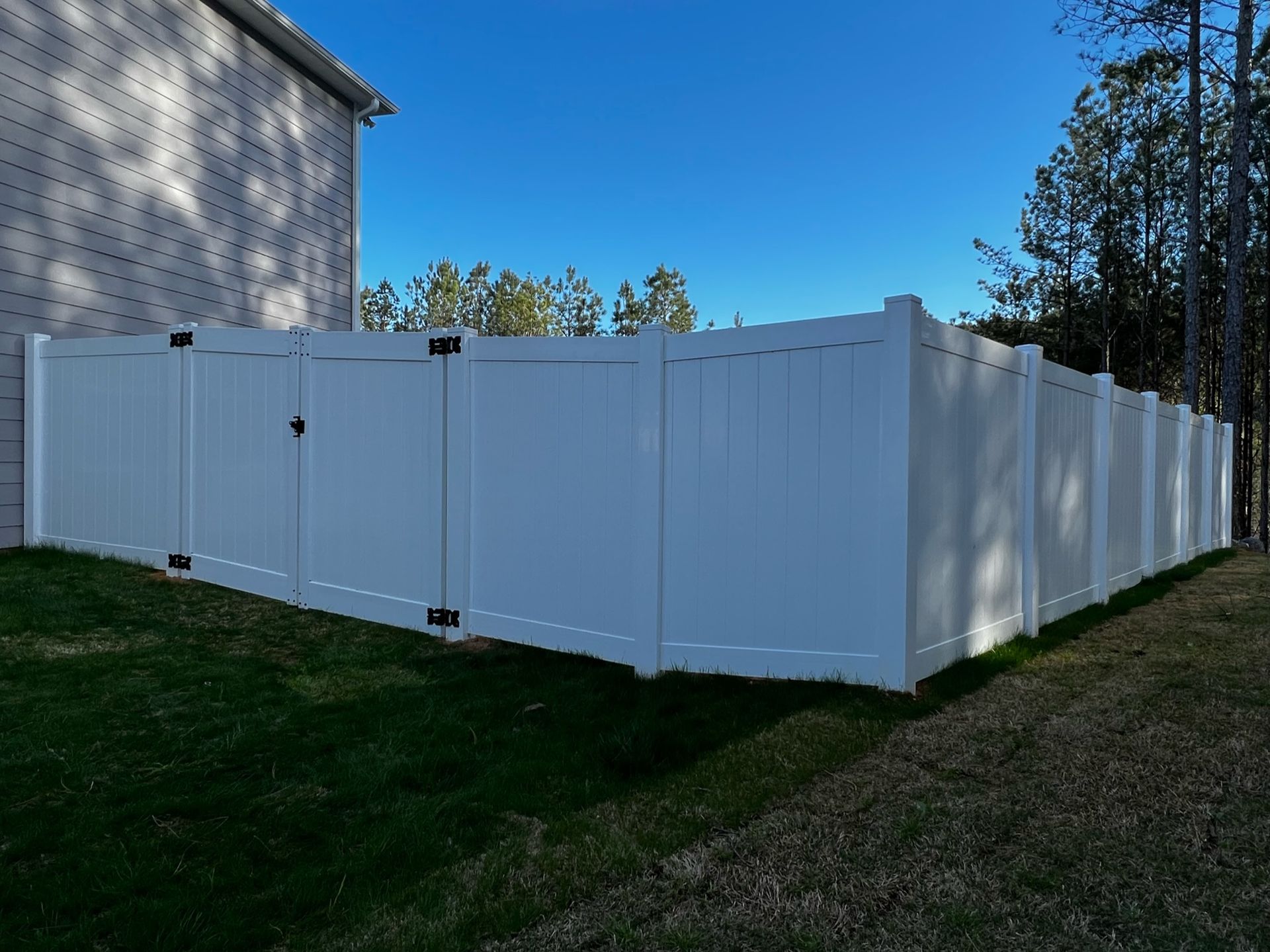 White vinyl fence enclosing a grassy yard, with a blue sky background.