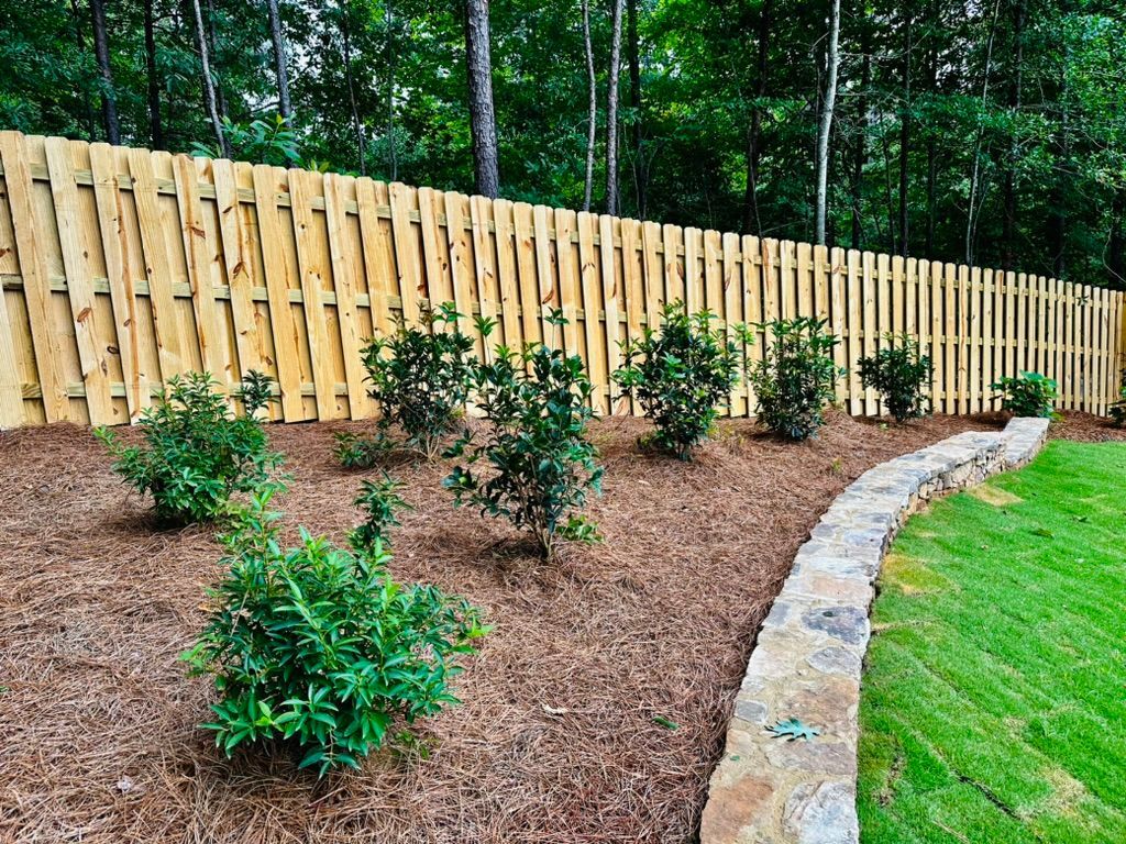 Wooden fence with small green bushes planted along a stone retaining wall.