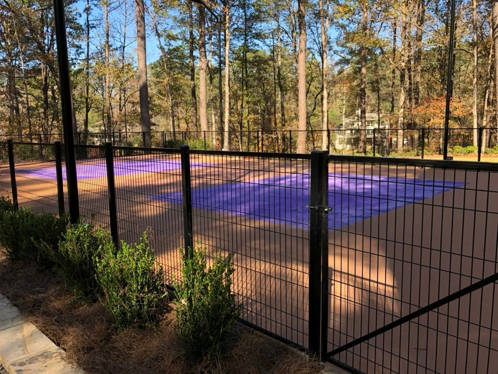 Black fenced enclosure with purple and brown surface surrounded by trees.