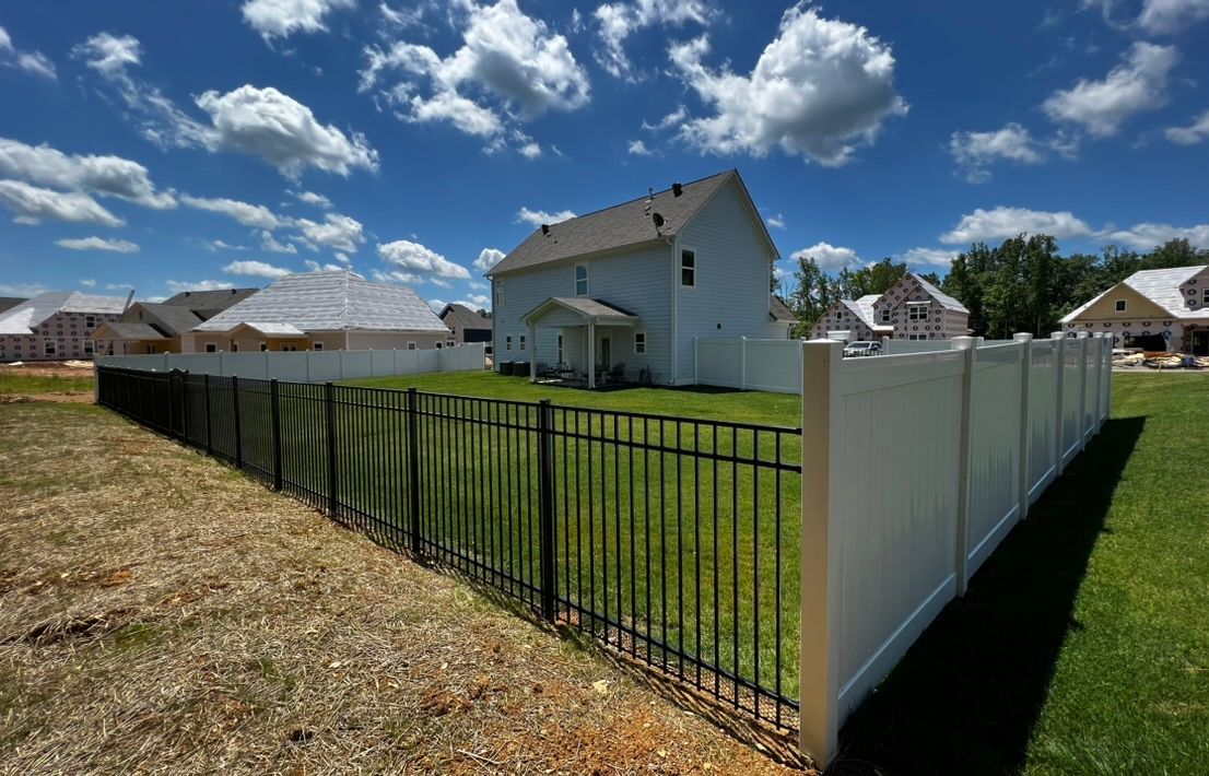 A house with a black metal fence in front and a white fence on the side, under a blue sky.