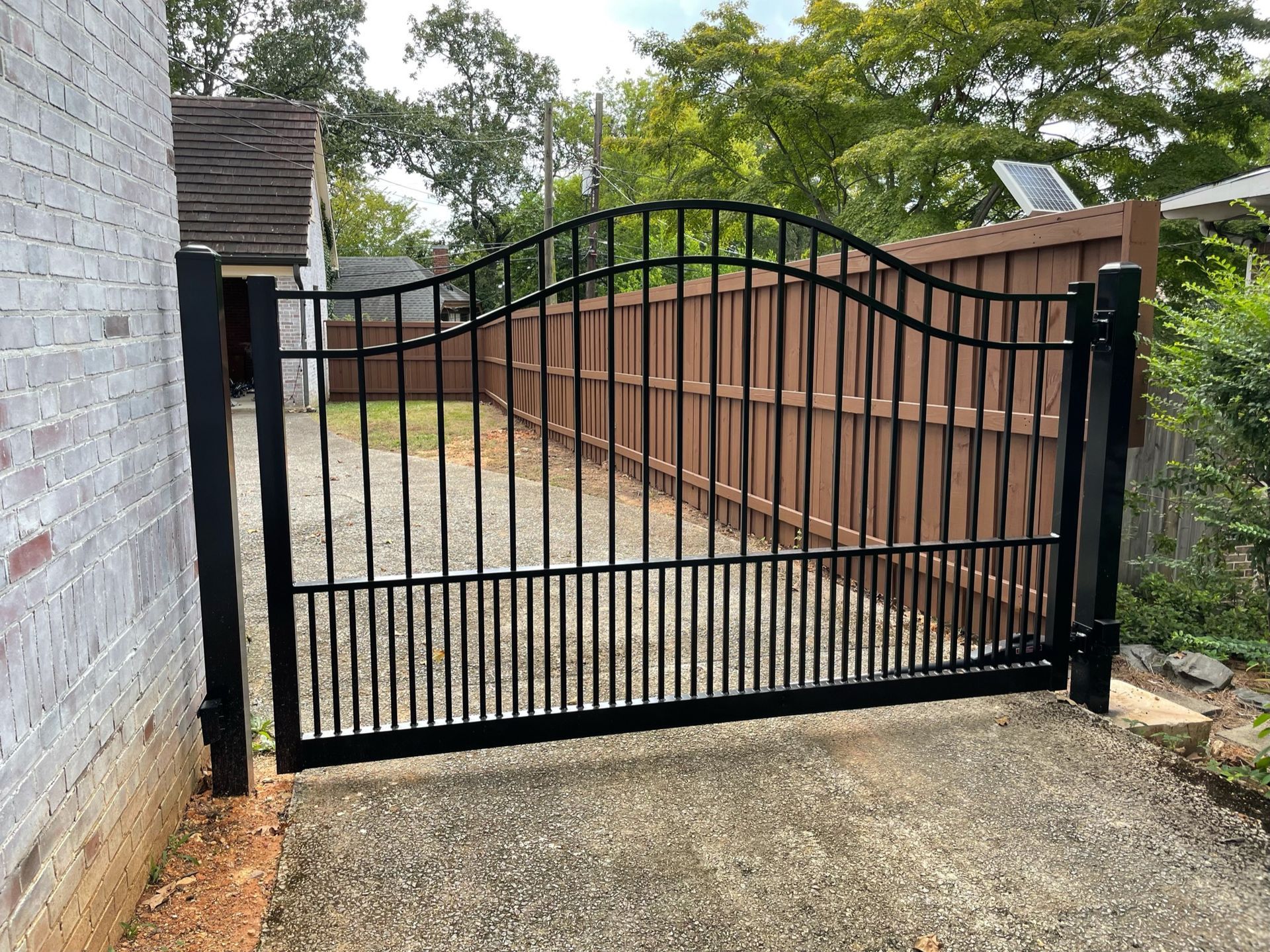 Black wrought iron gate in front of a gravel driveway. Behind it is a wooden fence.